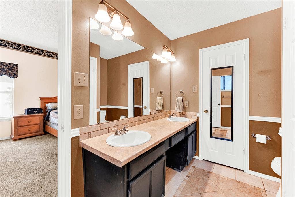 A spacious vanity area with double sinks and vanity lights provides optimal space and function. Morning routines become smooth and enjoyable as two people comfortably prepare for the day side-by-side.