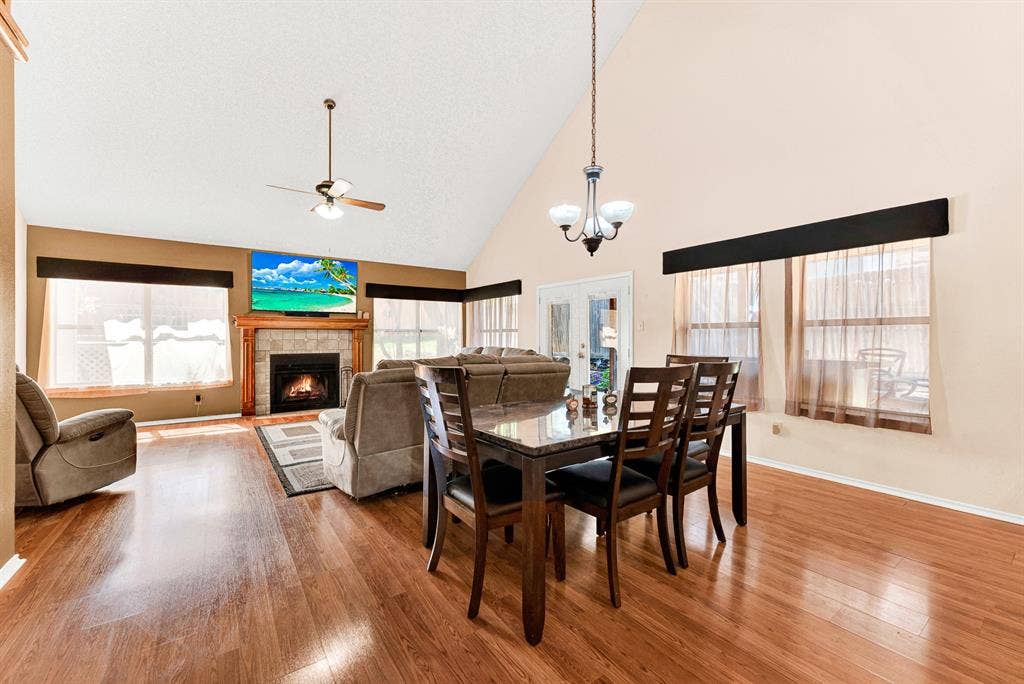 A classic chandelier anchors this open dining space beneath a soaring pitched ceiling, while expansive windows bathe the room in warm natural light. Picture hosting weekend dinner parties where lively conversation easily spills over into the adjoining living room.