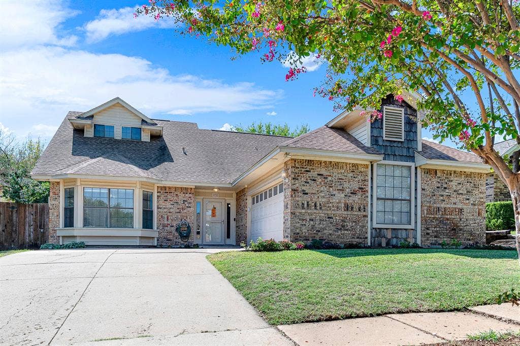 A mature flowering crape myrtle frames the manicured lawn and multi-textured exterior walls. It sets the scene for welcoming neighbors or stepping out on a breezy afternoon to enjoy the curb appeal.
