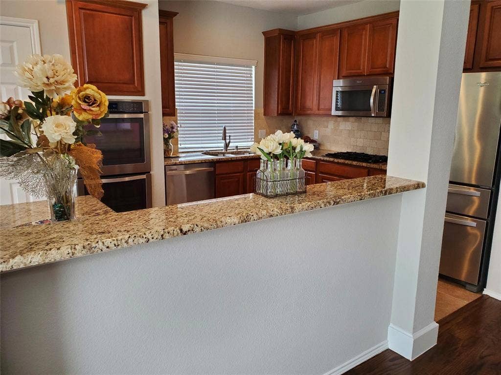 2077 Sleepy Hollow Trail, Frisco, TX 75033 Kitchen featuring dark wood-type flooring, appliances with stainless steel finishes, sink, tasteful backsplash, and light stone counters