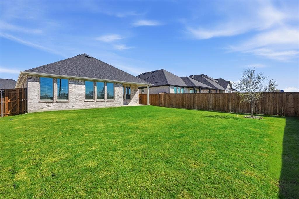 Expansive lawn featuring a privacy fence, a mature tree, and a light-colored brick exterior