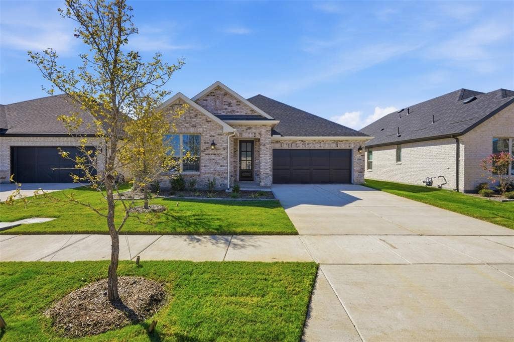 Brick façade with dark trim accents, attached two-car garage, concrete driveway, and front lawn