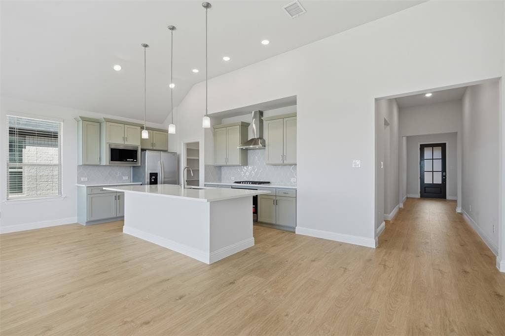 Vaulted ceiling, recessed lighting, wood-finish flooring, central kitchen island, and light-toned cabinetry