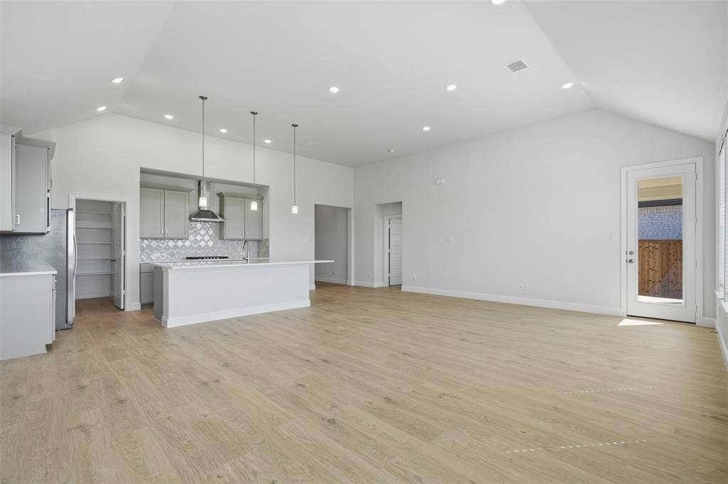Open-concept living area with vaulted ceilings, wood-finish flooring, recessed lighting, and a glass-paneled door