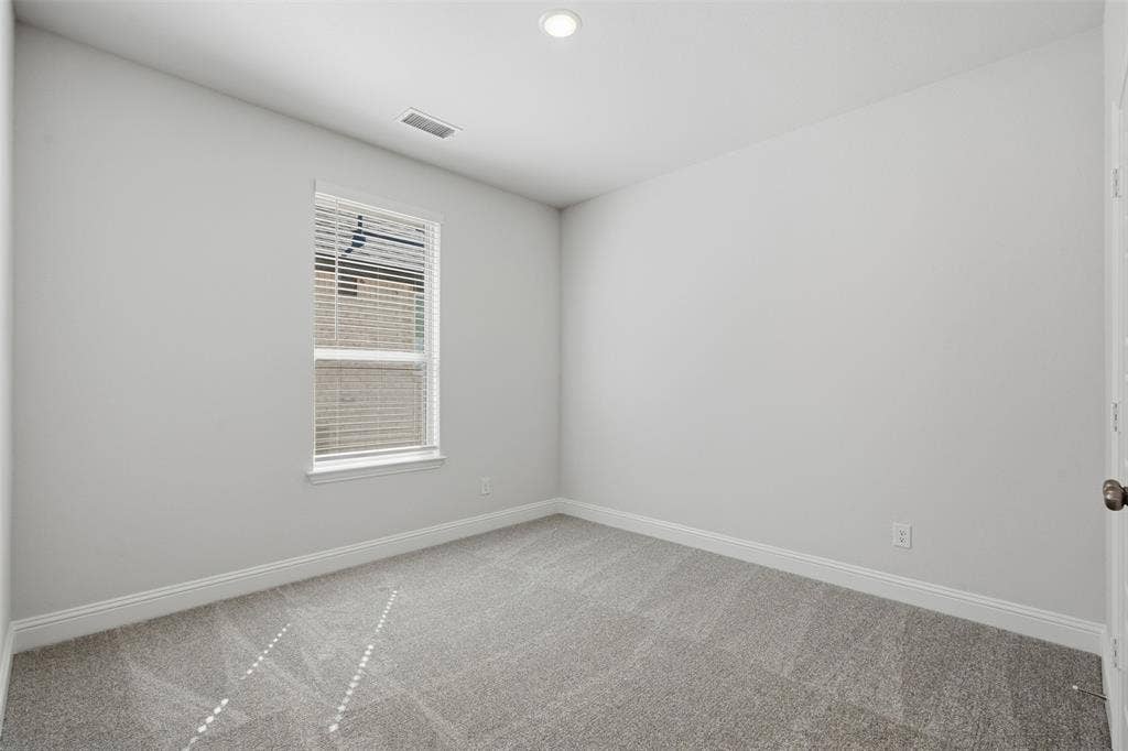 Recessed ceiling lighting illuminates a room featuring light gray carpeting and white painted walls
