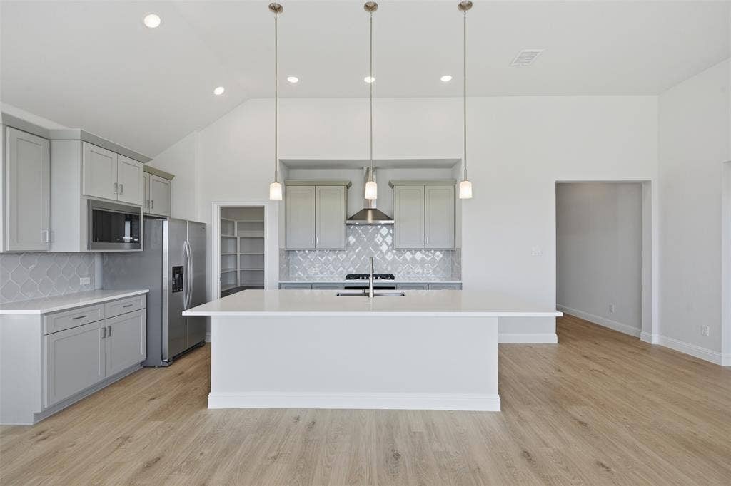 Spacious kitchen featuring an expansive island, light wood-finish flooring, recessed lighting, and a patterned tile backsplash