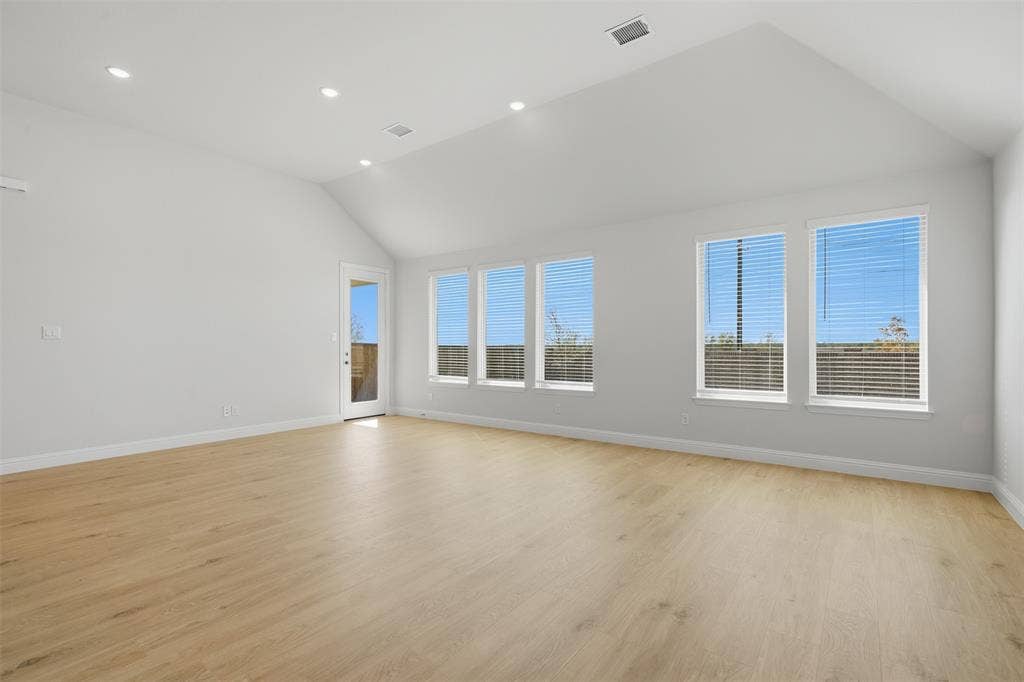 Vaulted ceiling, recessed lighting, wood-finish flooring, multiple windows with blinds, and a glass-panel door