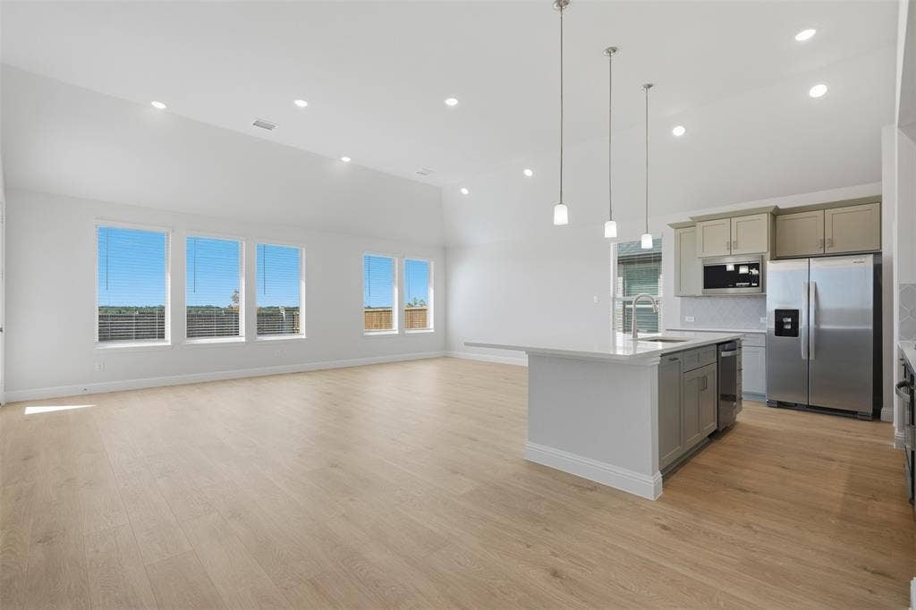 Open-concept living space with wood-finish flooring, vaulted ceilings, recessed lighting, and large windows