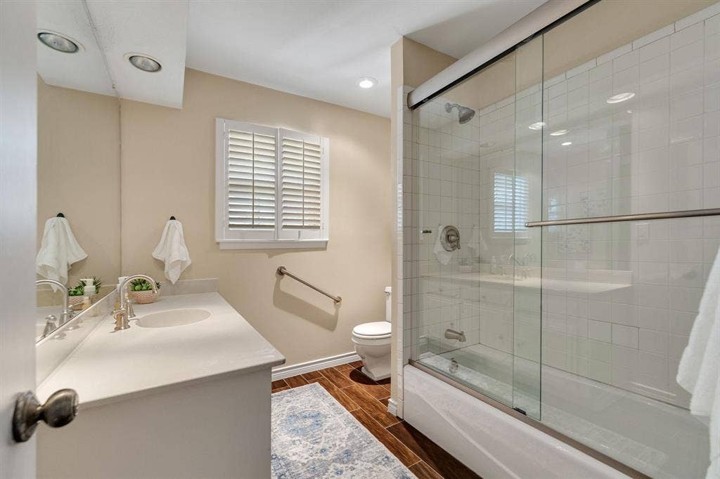 824 Westwood Drive, Richardson, TX 75080 The guest bathroom is a great size and features wood like ceramic tile, a large vanity and a tub-shower combination with a sliding glass door and white tile surround.
