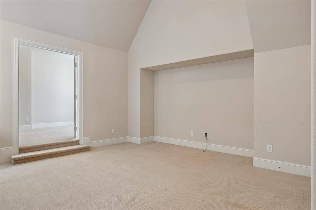 Vaulted ceiling, neutral tone carpeting, recessed wall niche, and crisp white trim