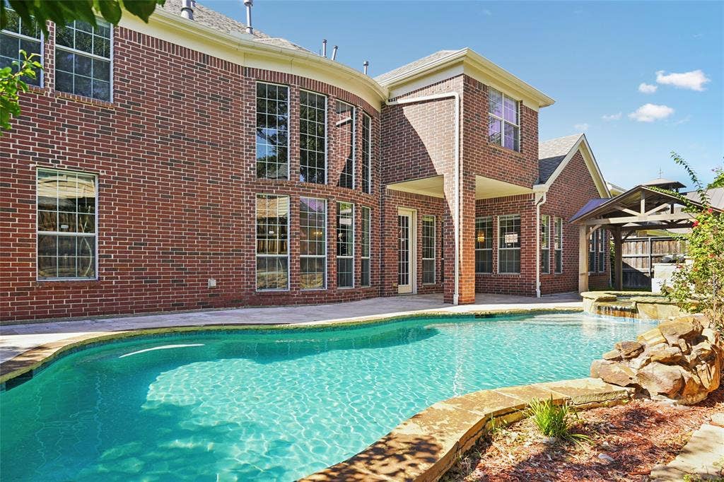 Brick exterior with multiple large windows, a freeform swimming pool, and an integrated spa with rock detailing