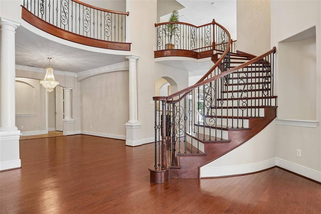 Grand entryway featuring a curved staircase, wrought iron balusters, rich wood-finish flooring, and architectural columns