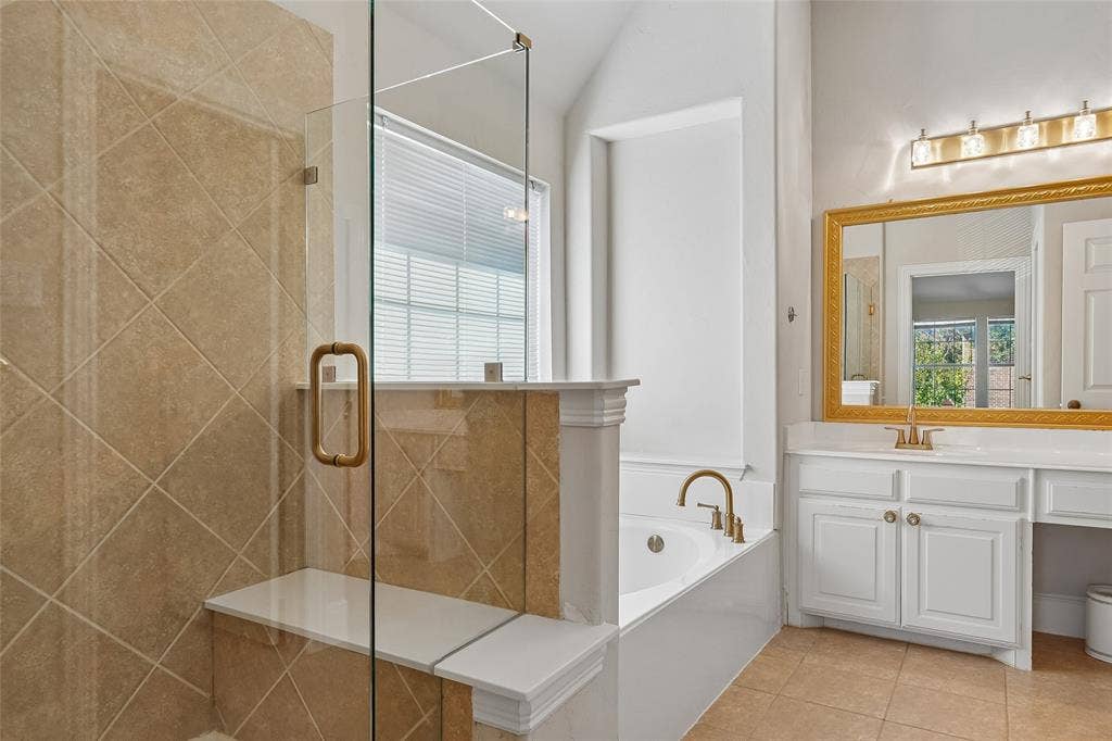 Glass-enclosed shower with a built-in bench, beige diagonal tile, and gold-tone hardware