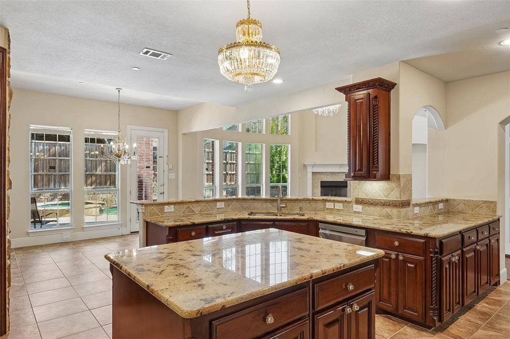 Spacious kitchen featuring an expansive island, granite countertops, decorative wood cabinetry, and tile flooring