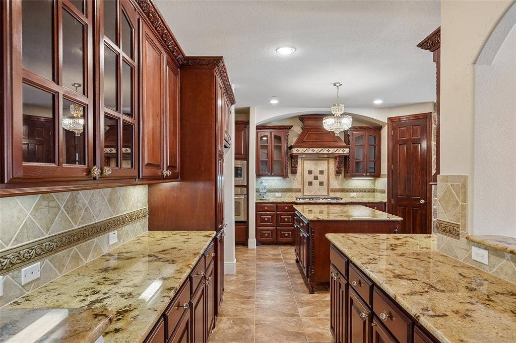 Kitchen featuring wood cabinetry, granite countertops, decorative tile backsplash, and a central island