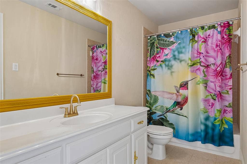 White vanity with gold-tone hardware, rectangular sink, gold-tone faucet, and large framed mirror