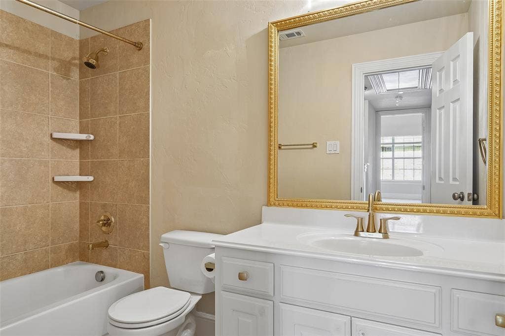 White vanity with a single basin sink, gold-finish faucet, and a large framed mirror
