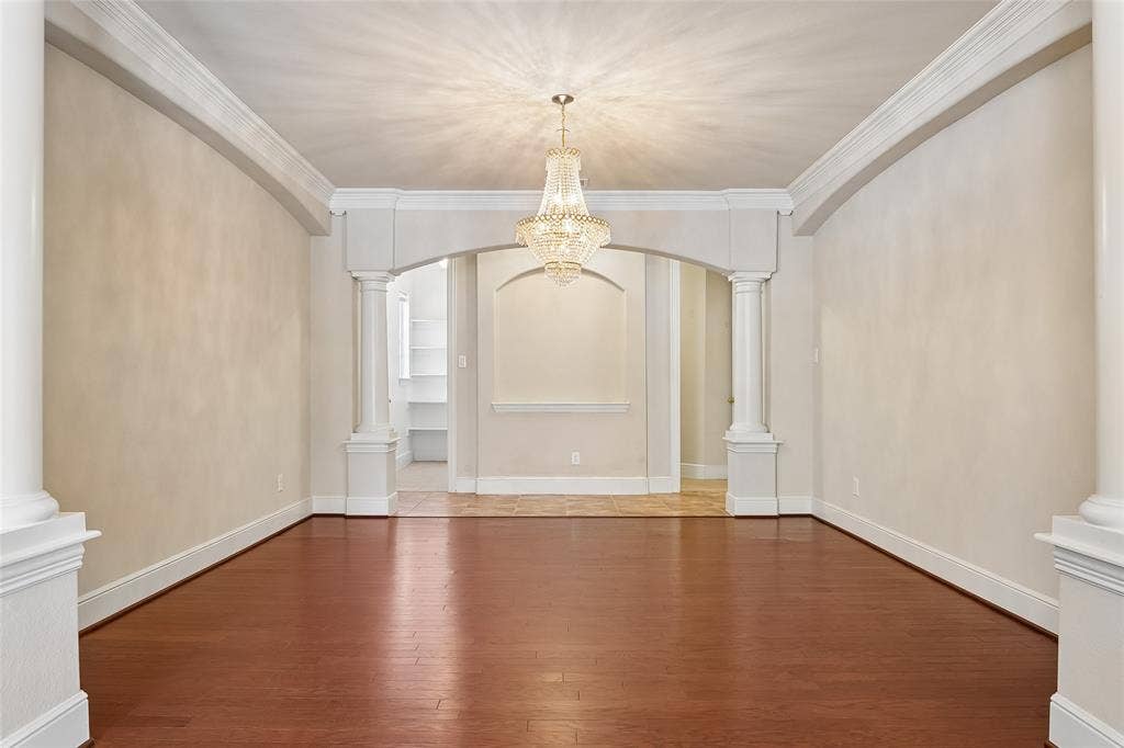 Hardwood flooring, decorative chandelier, arched entryway, architectural columns, and crown molding