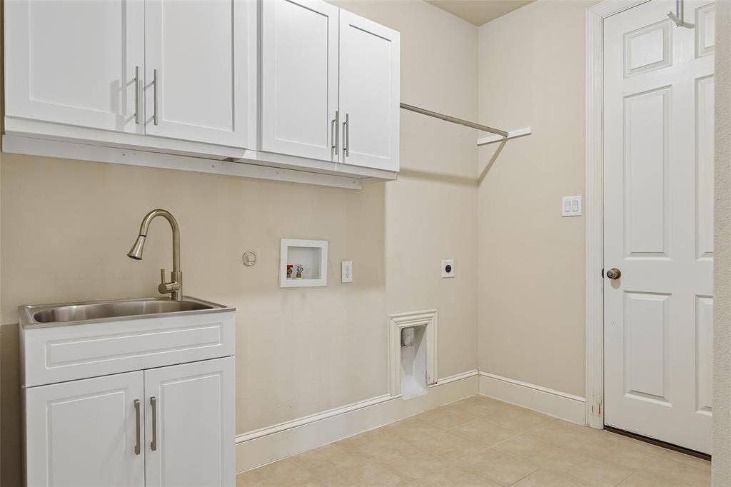 Laundry area featuring overhead white shaker cabinetry, an undermount stainless steel sink with a gooseneck faucet, a built-in hanging rod, and tile flooring