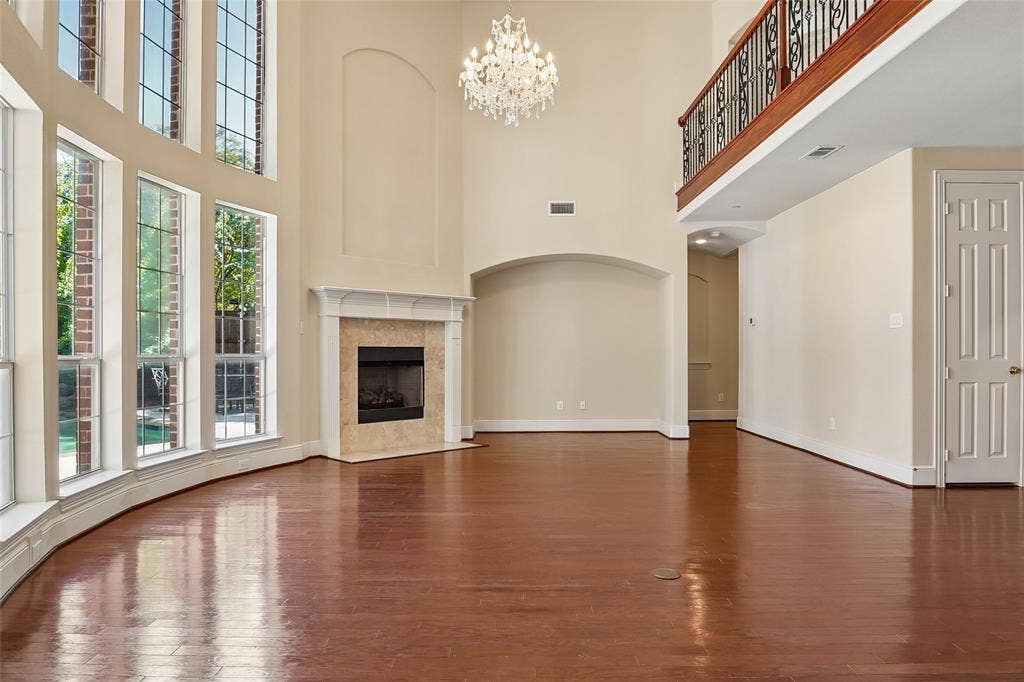 Hardwood flooring, high ceilings, decorative chandelier, fireplace with stone surround, and a second-story balcony with an iron railing