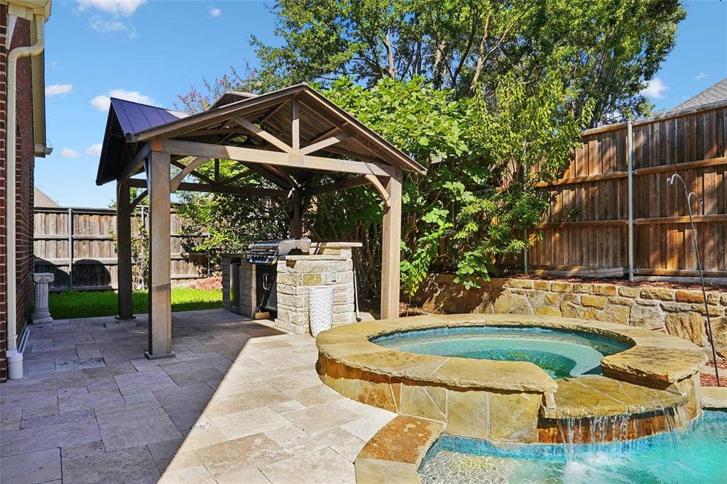 Stone paver patio featuring a covered outdoor kitchen, built-in grill, and a spa with a waterfall feature