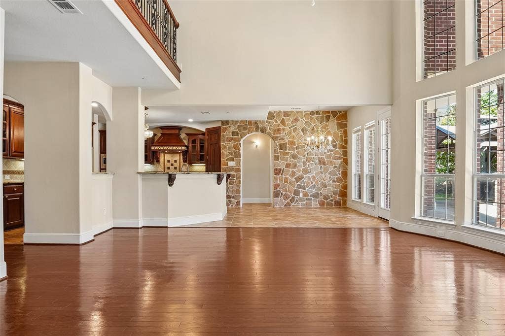 Hardwood flooring throughout, stone accent wall, high ceilings, large windows, and a second-story balcony
