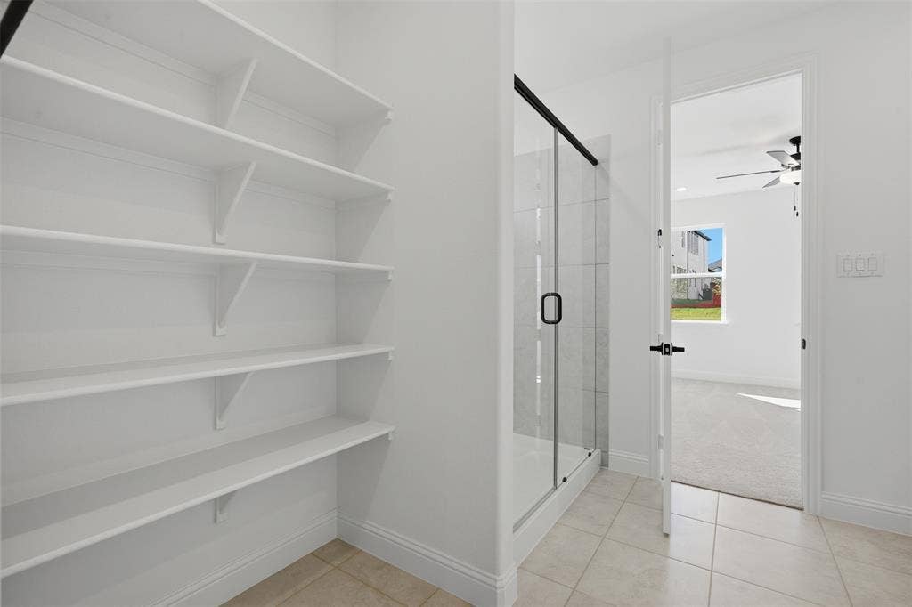 Built-in shelving, glass-enclosed shower with black trim, and light tile flooring