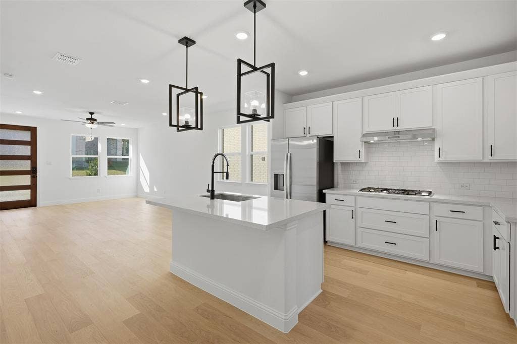 Kitchen featuring white cabinetry, subway tile backsplash, stainless steel appliances, and a central island with a sink