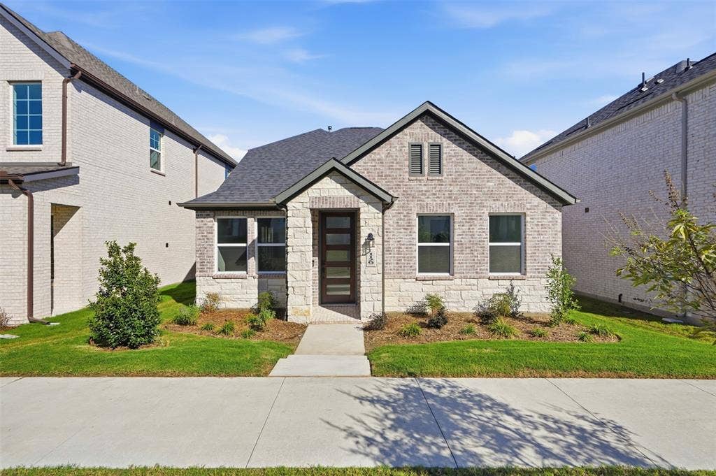 Brick and stone veneer exterior with a dark shingle roof, featuring a modern entry door with horizontal lites, and framed windows