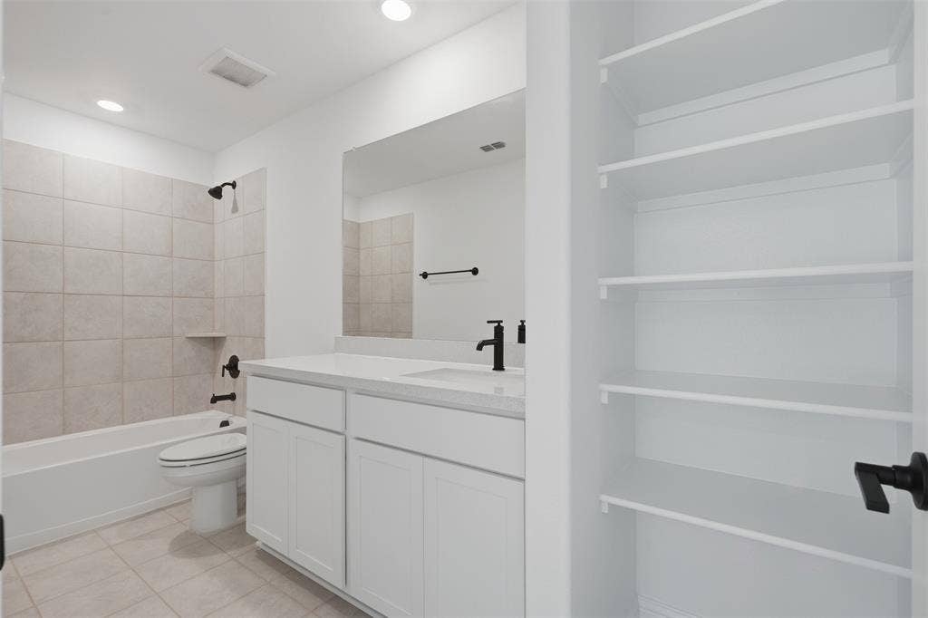 White cabinetry with a white countertop and rectangular sink, matte black fixtures, tile flooring, built-in shelving, and a tiled shower-tub combination