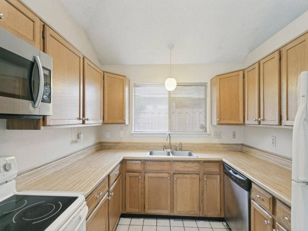 714 Bluebonnet Drive, Allen, TX 75002 Kitchen featuring wood cabinetry, laminate countertops, stainless steel appliances, double-basin sink, and tiled flooring