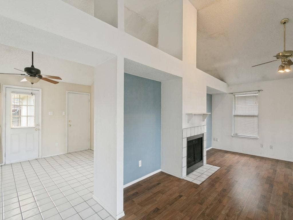 714 Bluebonnet Drive, Allen, TX 75002 High-ceiling living area featuring wood-finish flooring, a tile-surround fireplace with a mantel, clerestory-style shelving, and two ceiling fans