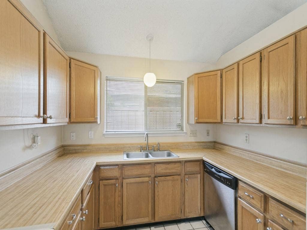 714 Bluebonnet Drive, Allen, TX 75002 Kitchen featuring wood cabinetry, integrated laminate countertops with matching backsplash, stainless steel double-basin sink with gooseneck faucet, built-in dishwasher, and a globe pendant light fixture