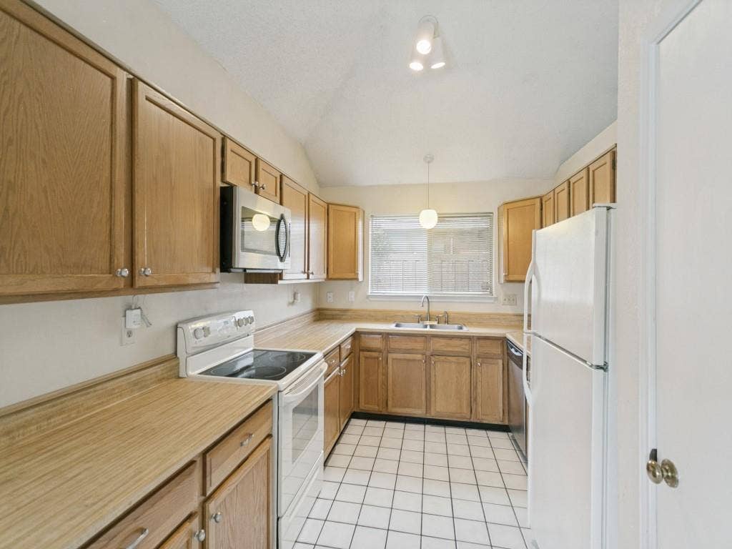 714 Bluebonnet Drive, Allen, TX 75002 Kitchen featuring oak cabinetry, laminate countertops, stainless steel microwave, tile flooring, and vaulted ceiling