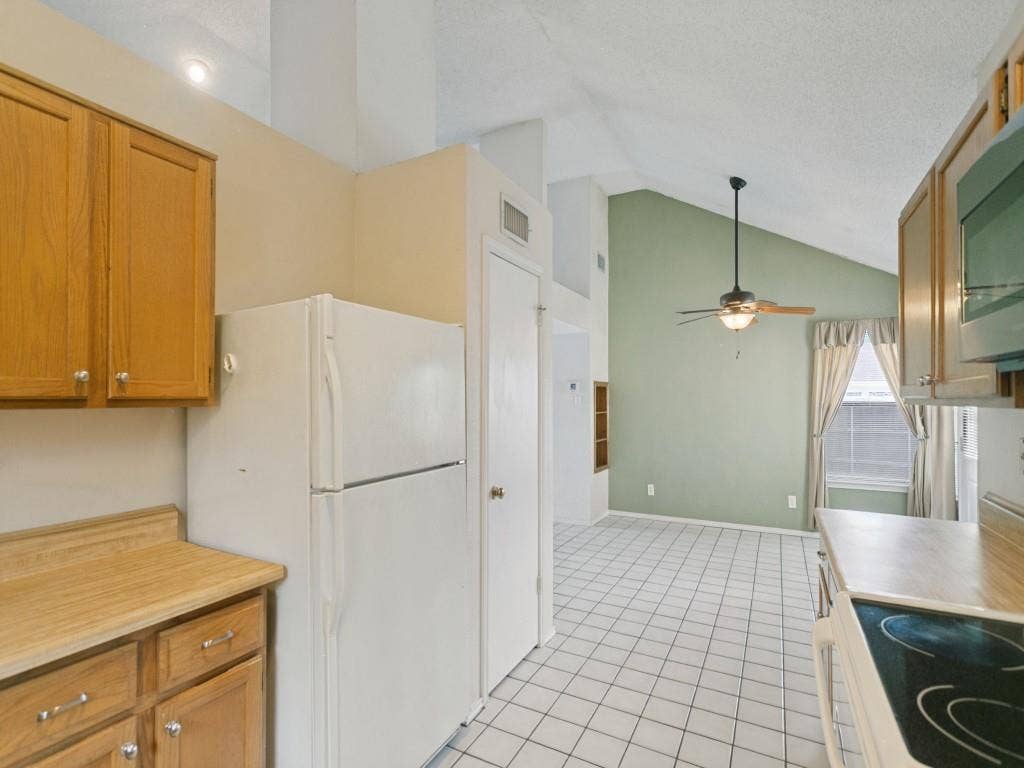 714 Bluebonnet Drive, Allen, TX 75002 Kitchen featuring wood cabinetry, laminate countertops, a smooth-top electric range, tiled flooring, and a vaulted ceiling with a built-in ceiling fan- Fridge to convey