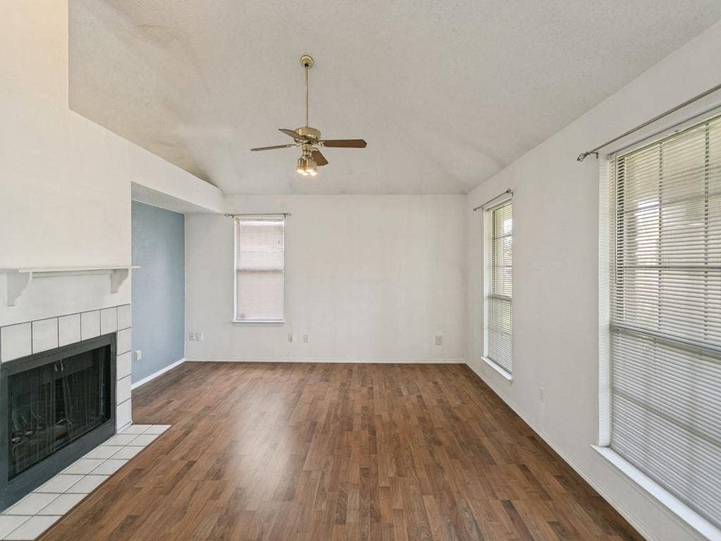 714 Bluebonnet Drive, Allen, TX 75002 Vaulted ceiling featuring a central light-integrated ceiling fan, wood-finish flooring, and a fireplace with a ceramic tile surround and mantel