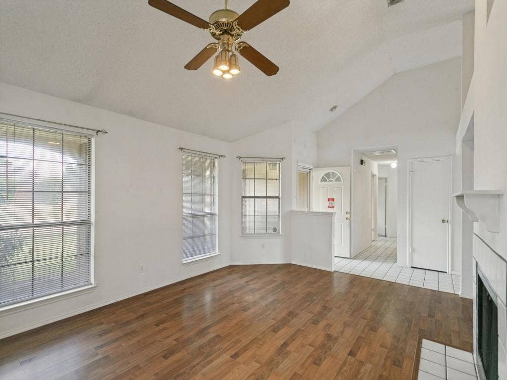 714 Bluebonnet Drive, Allen, TX 75002 Vaulted ceiling with a central multi-light fan, wood-finish flooring, grid-pattern windows, and a tiled fireplace surround