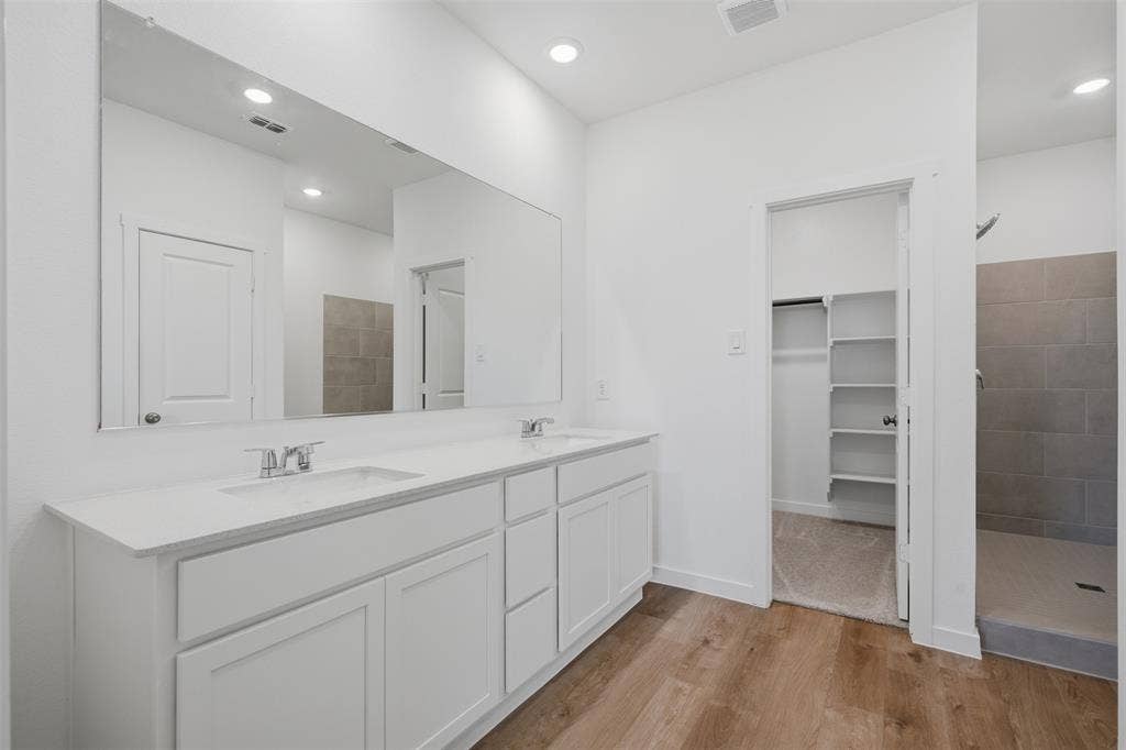 7117 Black Cherry Lane, McKinney, TX 75071 Double vanity with white cabinetry and integrated sinks, wide-plank wood-finish flooring, recessed lighting, and a walk-in shower with large format tile