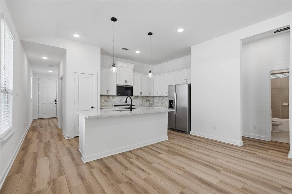 Open-concept kitchen with white cabinetry, stainless steel appliances, and wood-finish flooring