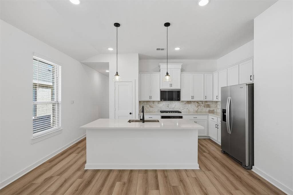 Kitchen featuring a large central island, pendant lighting, stainless steel appliances, white cabinetry, and wood-finish flooring