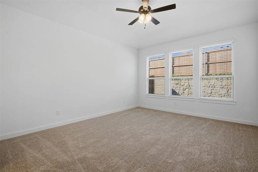 Three large windows with blinds, ceiling fan with integrated lighting, and neutral carpeting