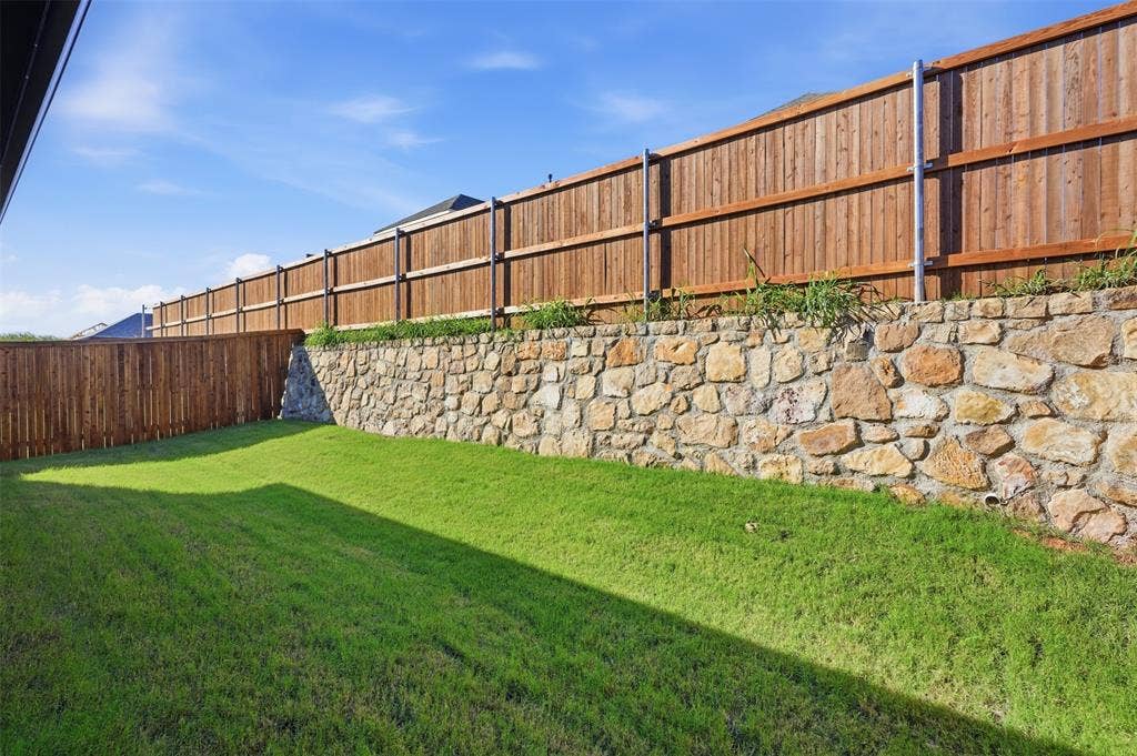 Expansive backyard featuring a stone retaining wall, level lawn, and perimeter wood fencing