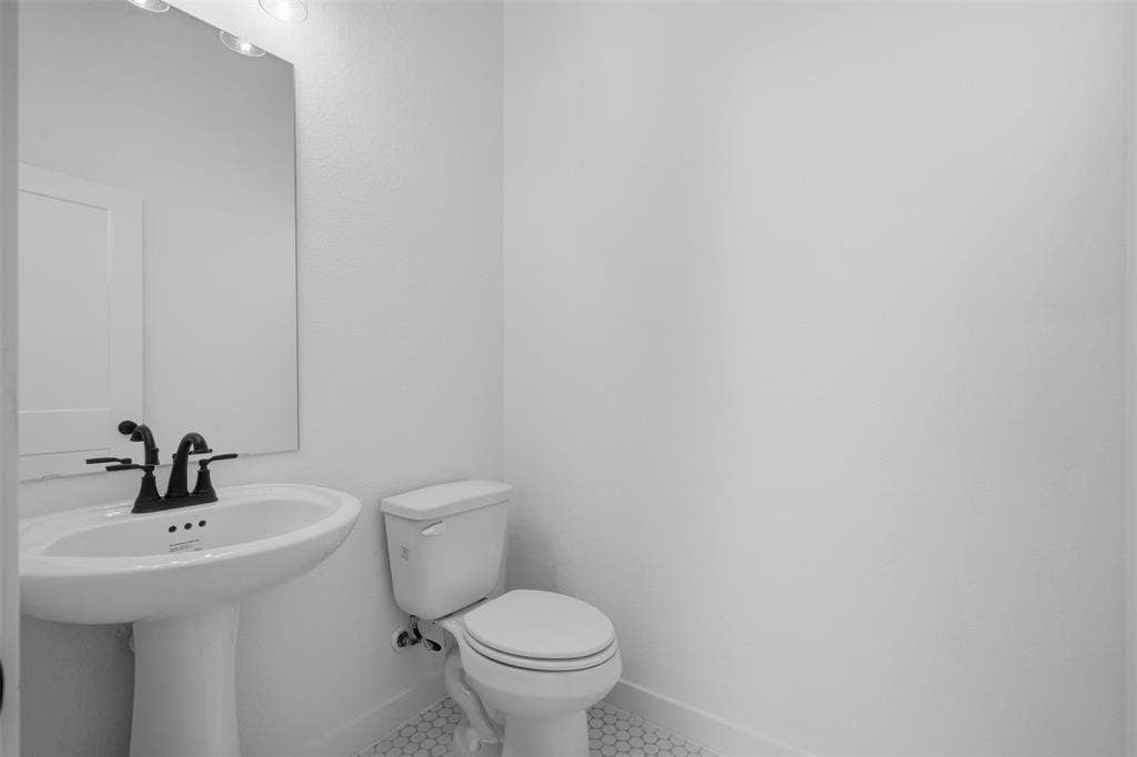 Pedestal sink with a matte black faucet, mirrored vanity, and hexagonal tile flooring
