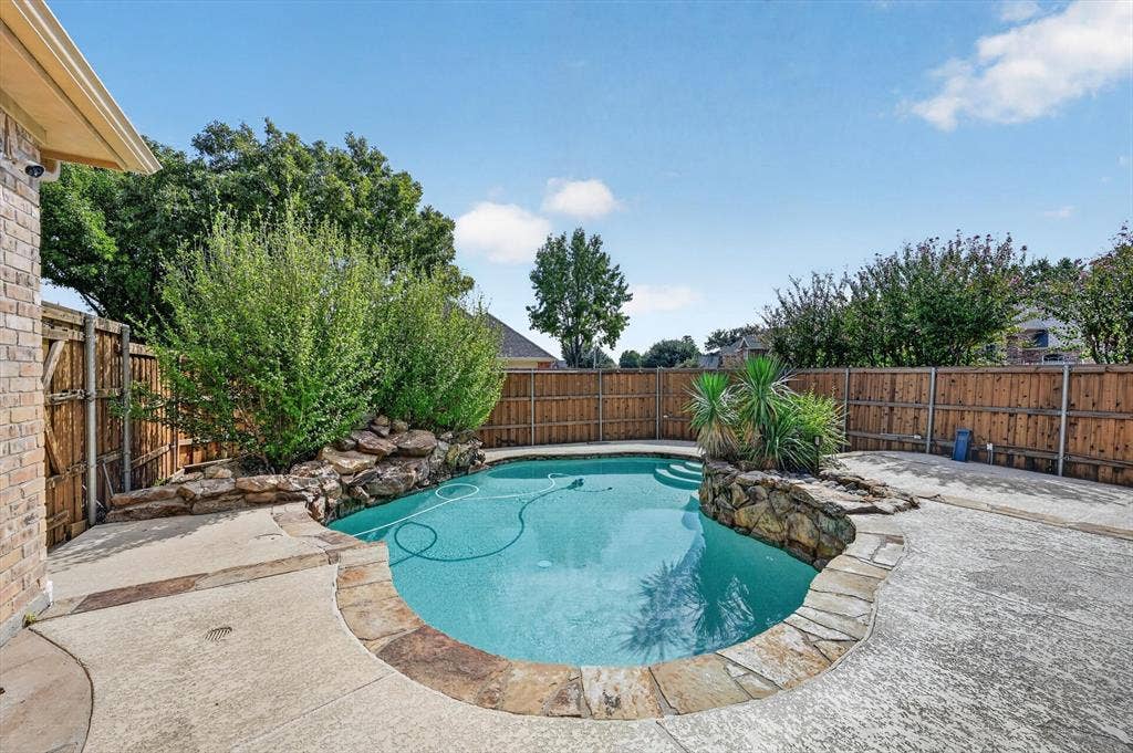 512 Renfro Court, Irving, TX 75063 In-ground swimming pool featuring stone accents, integrated rock landscaping, a stone coping perimeter, and surrounding concrete decking enclosed by wood fencing