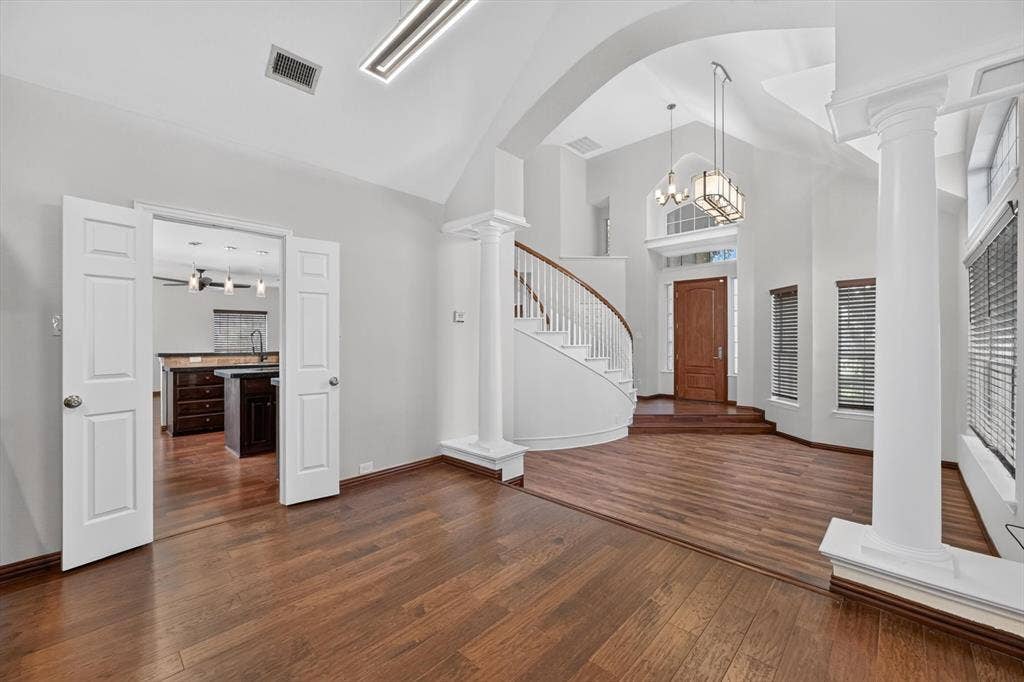 512 Renfro Court, Irving, TX 75063 Open-concept floor plan featuring vaulted ceilings, wood-finish flooring, a curved staircase with a wooden handrail, classic structural columns, and a multi-paneled wood entry door