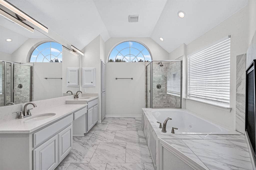 512 Renfro Court, Irving, TX 75063 Bathroom featuring a dual-sink vanity with white cabinetry, quartz-surface countertops, arched window, soaking tub, and a glass-enclosed shower with stone-tile surround