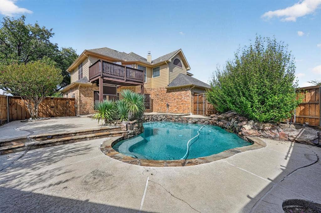 512 Renfro Court, Irving, TX 75063 Exterior backyard featuring a stone-lined pool, elevated deck, multi-level concrete patio, and perimeter wood fencing