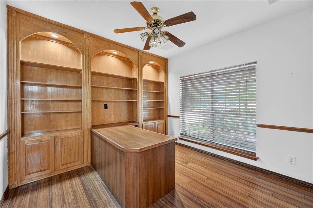 512 Renfro Court, Irving, TX 75063 Built-in oak cabinetry with arched shelving, integrated lighting, wood-finish flooring, and a central workspace desk
