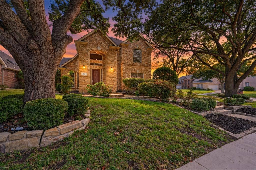 512 Renfro Court, Irving, TX 75063 Brick exterior featuring an arched entryway, stone-bordered landscape beds, and mature shade trees