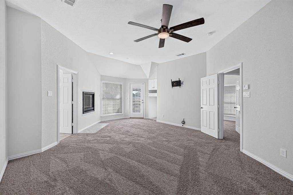 512 Renfro Court, Irving, TX 75063 Vaulted ceiling featuring a central five-blade ceiling fan, wall-mounted gas fireplace, neutral wall-to-wall carpeting, and a glass-paneled exterior door